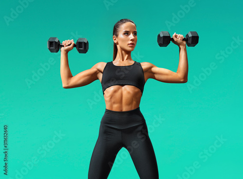 Beautiful young woman doing exercises with dumbbells. Photo athletic woman with perfect body on turquoise background. Strength and motivation © Romario Ien