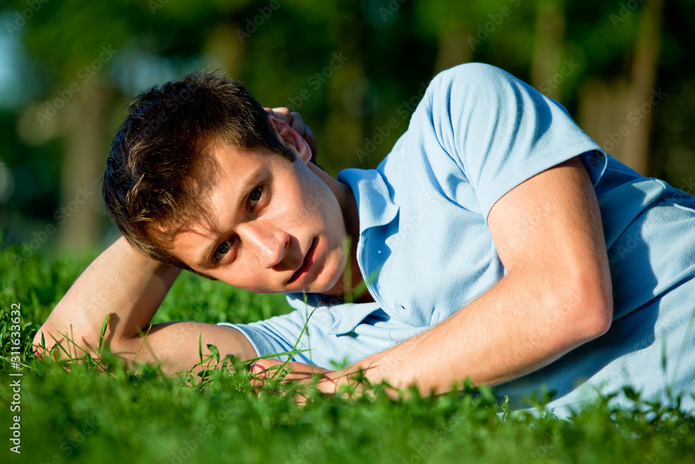 Young man in casual clothing lying on green grass and looking at camera