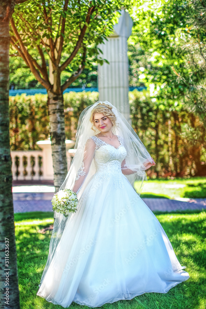 Young bride wearing gorgeous wedding dress, playing with veil. plays a wedding dress. Dress develops in the wind. Happy blonde bride in park