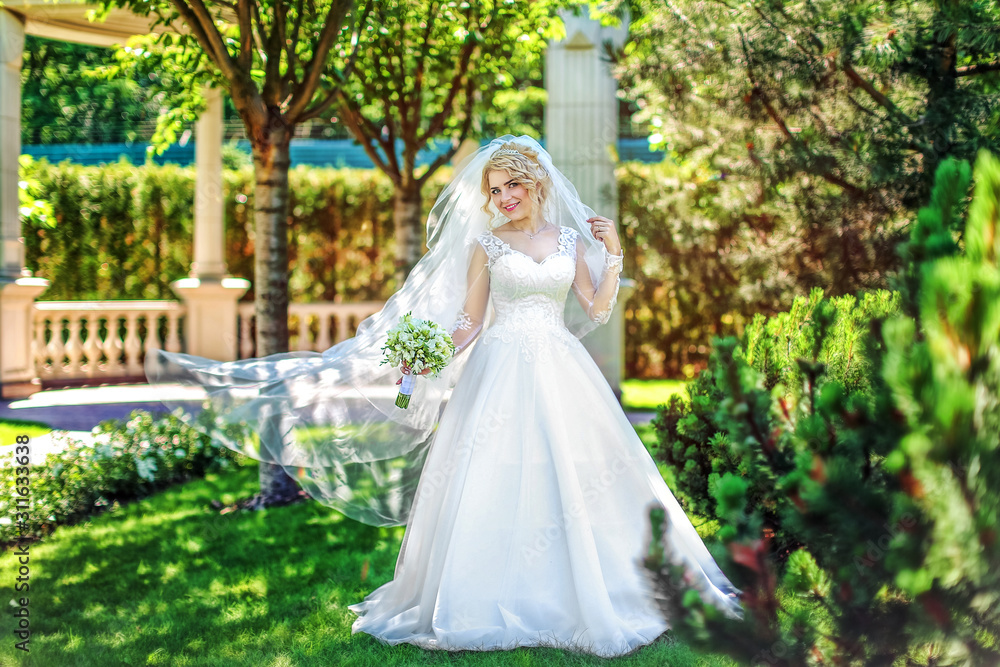 Young bride wearing gorgeous wedding dress, playing with veil. plays a wedding dress. Dress develops in the wind. Happy blonde bride in park Young bride wearing gorgeous wedding dress, playing with veil. plays a wedding dress. Dress develops in the wind. Happy blonde bride in park