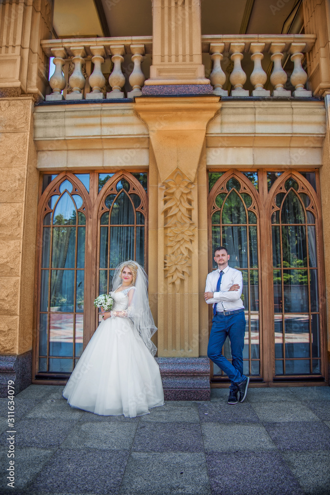 Stylish groom holds a veil  beautiful and smiling blonde bride. Wedding portrait of lovers newlyweds near vintage windows