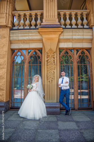 Stylish groom holds a veil beautiful and smiling blonde bride. Wedding portrait of lovers newlyweds near vintage windows