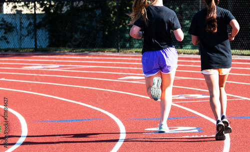 Two high school girls running on the turn on a track