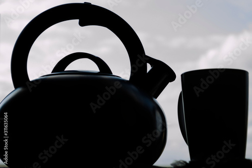 Steel tea kettle and mug. Hot morning tea in clay white mug and kettle on wooden breakfast table