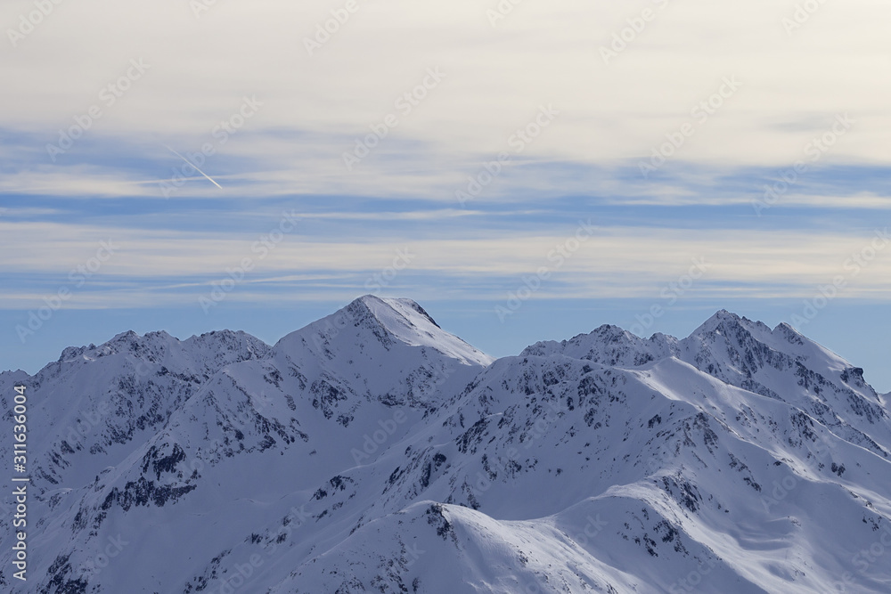 Snowy slope in high winter mountains and sunlit cloudy sky at evening Snowy slope in high winter mountains and sunlit cloudy sky at evening