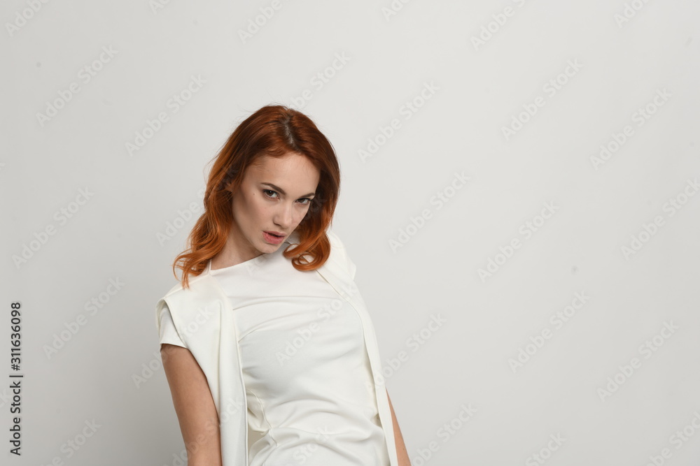 Beautiful redhead girl in a beige dress posing in front of the camera. Portrait on a neutral light background, space for text. Beautiful redhead girl in a beige dress posing in front of the camera. Portrait on a neutral light background, space for text.