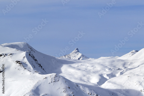 Snowy off piste ski slope, sunlit plateau and peak at high winter mountains