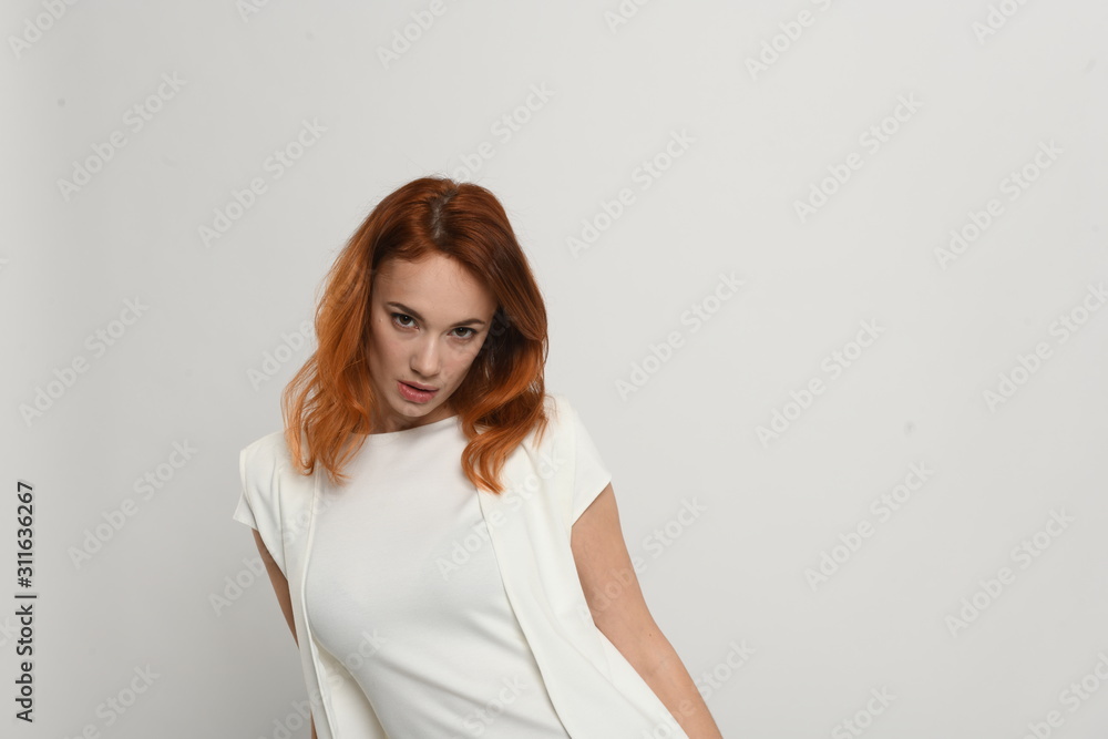 Beautiful redhead girl in a beige dress posing in front of the camera. Portrait on a neutral light background, space for text. Beautiful redhead girl in a beige dress posing in front of the camera. Portrait on a neutral light background, space for text.