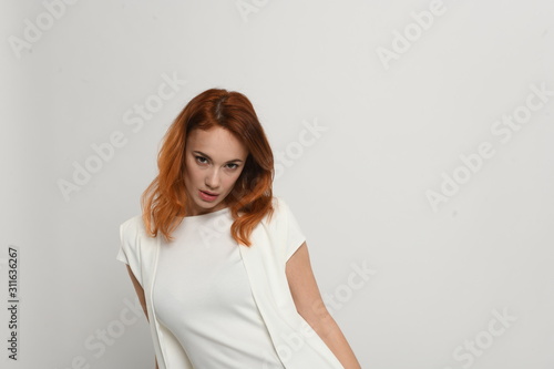Beautiful redhead girl in a beige dress posing in front of the camera. Portrait on a neutral light background, space for text. © atdigit