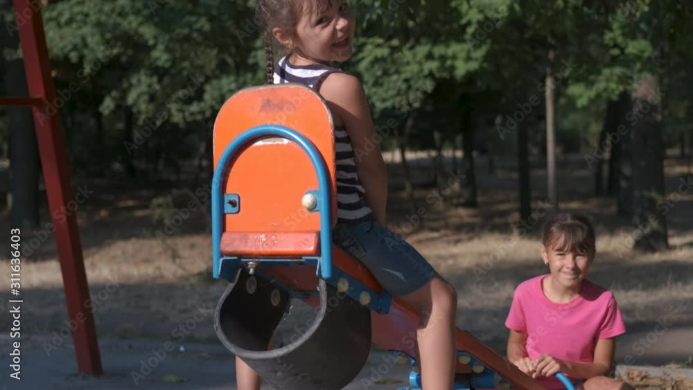 Children on a swing. On see saw swing. Cheerful little sisters ride a swing. Children on a swing. On see saw swing. Cheerful little sisters ride a swing.