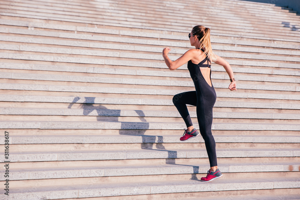 Full length back view of a young sportswoman dressed in sportswear running up the stairs outdoors Full length back view of a young sportswoman dressed in sportswear running up the stairs outdoors