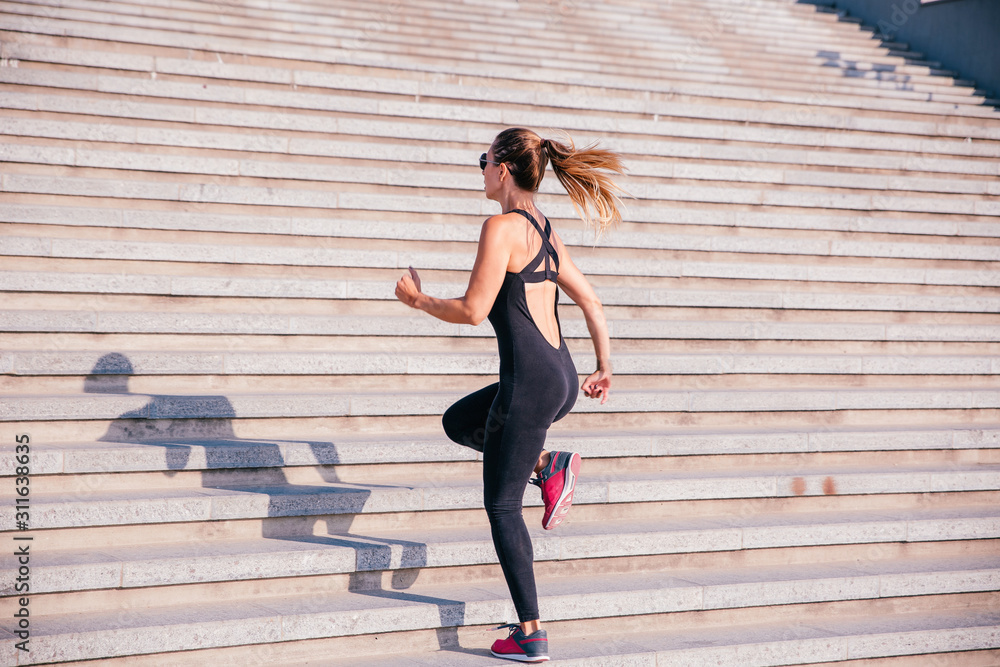 Full length back view of a young sportswoman dressed in sportswear running up the stairs outdoors Full length back view of a young sportswoman dressed in sportswear running up the stairs outdoors