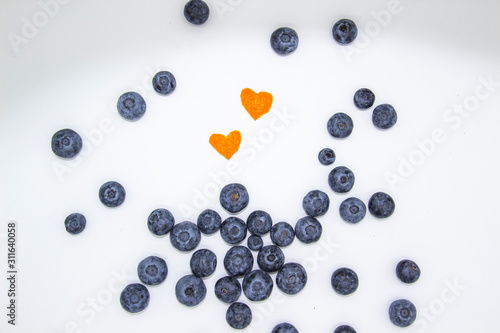 Fresh blueberry  with mandarin peel in form a heart on white background. A composition of the blueberries, mandarin peel which is organic and healthy. The berries full of vitamins.