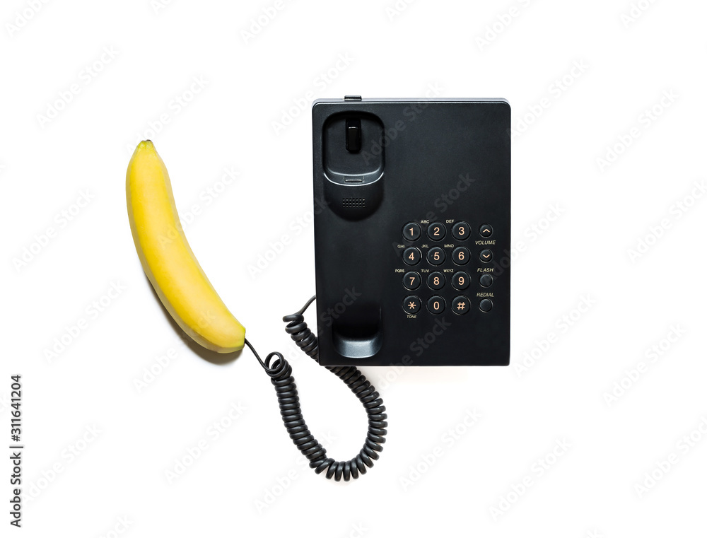 Creative photo of a simple modern black push-button telephone with a bright yellow banana instead of a handset close-up, isolated on a white background.