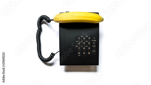 Creative photo of a simple modern black push-button telephone with a bright yellow banana instead of a handset close-up, isolated on a white background.
