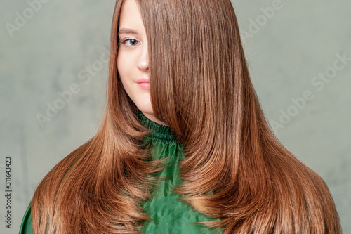 Portrait of beautiful young woman with long brown hairstyle on gray background.