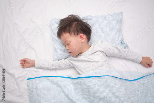 Cute little Asian 3 - 4 years old toddler boy kid in pajama taking a nap, sleeping on his back on white bed sheet in bed, Bedtime for kids concept with copy space photo