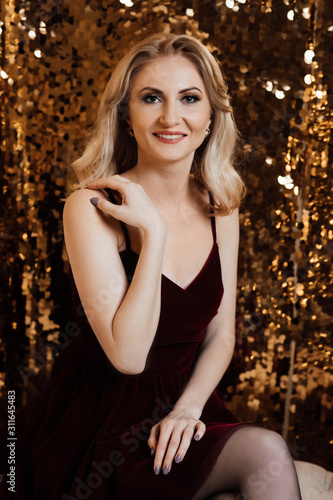 Christmas. Beautiful smiling woman. Makeup. Healthy long hair style. Elegant lady in dress over gold background. Happy new year. Fashion and vogue