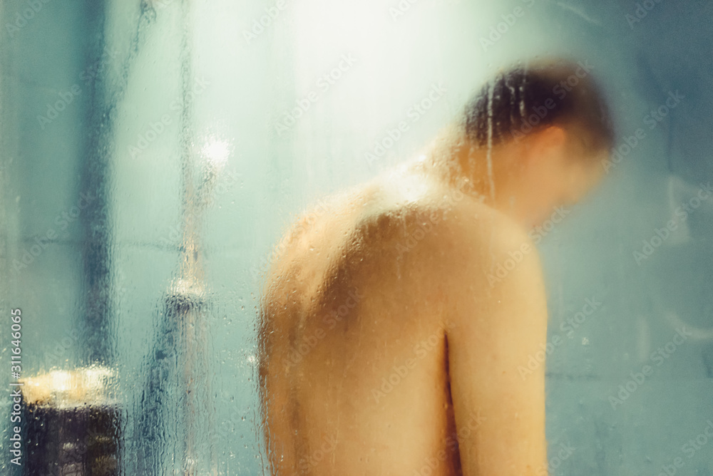 Blured shower background. Back view caucasian man washing in bathroom through steam glass.