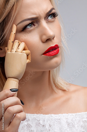 Attractive woman holding a wooden hand. Silence gesture. Blonde girl with red lips.