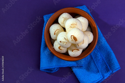 Indian Sweet or Dessert - Rasgulla, Famous Bengali sweet in clay bowl with blue napkin on violet background photo