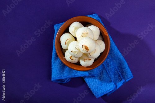 Indian Sweet or Dessert - Rasgulla, Famous Bengali sweet in clay bowl with blue napkin on violet background photo