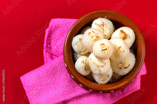 Indian Sweet or Dessert - Rasgulla, Famous Bengali sweet in clay bowl with napkin on Red Background photo