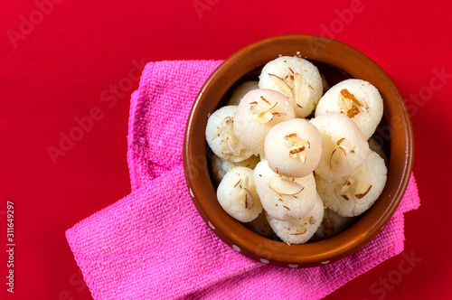 Indian Sweet or Dessert - Rasgulla, Famous Bengali sweet in clay bowl with napkin on Red Background