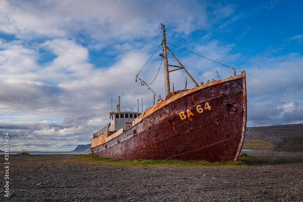 An out-of-the-way whaling ship that rusts on the road to Latrabjarg on a dead cloudy day. The shipwreck has the identification BA 64 and is located on a beach in the west of Iceland