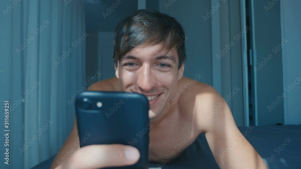 Young Naked Man Celebrating Success on Smartphone in Bed at Home in the Morning. Emotional Reacting to Winning. Young Naked Man Celebrating Success on Smartphone in Bed at Home in the Morning. Emotional Reacting to Winning.