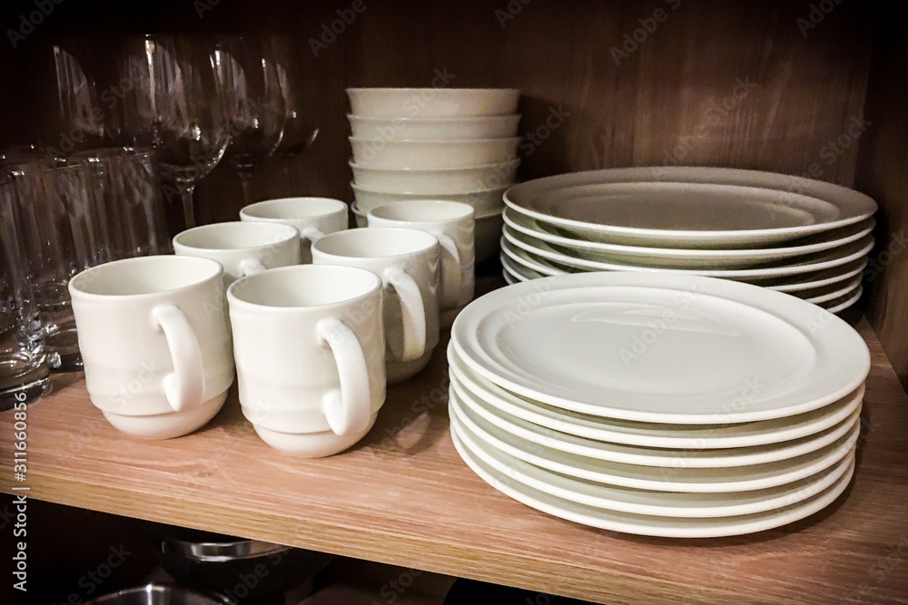 Kitchen utensils such as ceramic cups, plates, bowls, wine glasses, and drinking glasses were kept inside a wooden cabinet Kitchen utensils such as ceramic cups, plates, bowls, wine glasses, and drinking glasses were kept inside a wooden cabinet