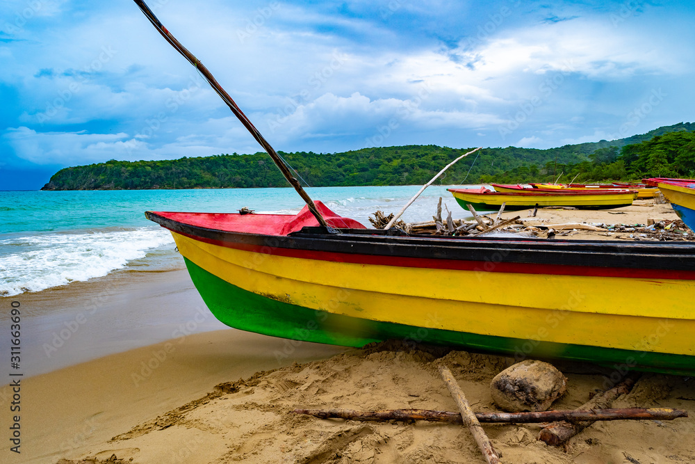 Fototapeta premium Colorful old wooden fishing boats docked by water on a beautiful beach coast. White sand sea shore landscape on tropical Caribbean island. Holiday weekend/ summer vacation setting in Jamaica.