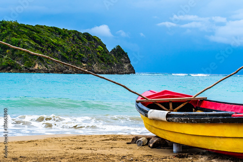 Colorful old wooden fishing boat docked by water on a beautiful beach coast. White sand sea shore landscape on tropical Caribbean island. Holiday weekend summer vacation setting in Jamaica.
