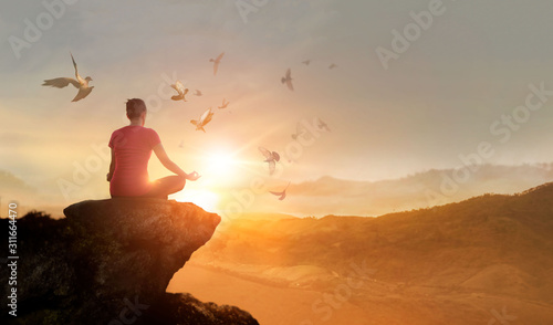Woman practices meditating and praying with free bird enjoying nature on the mountain sunset background, hope and faith concept.