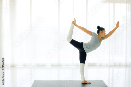 Side view of Beautiful Asian woman practicing yoga, standing in Natarajasana exercise, Lord of the Dance pose, working out, wearing sportswear,full length,indoor,lifestyle healthy concept.