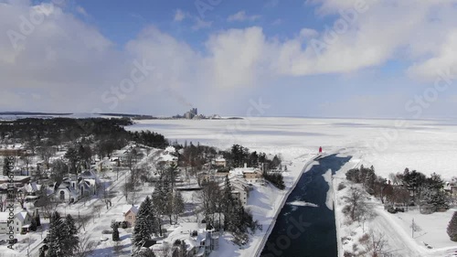 Winter in Northern Michigan in Charlevoix Lake Michigan and the Pine River meet downtown 4K drone shots over forest and open woods in winter snow covered scene lighthouse looking out to big lake photo