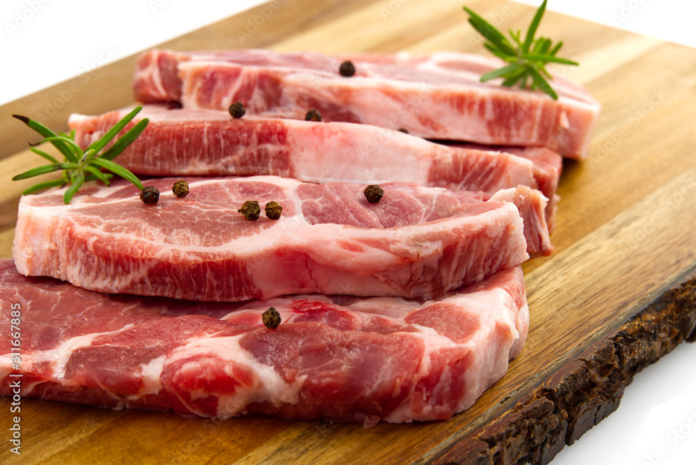 raw pork steak on wood cutting board. Pork with spices: rosemary and pepper. Close-up raw pork steaks.