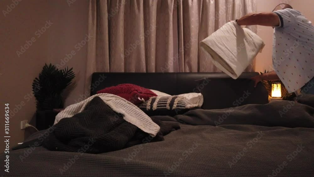 man making the right side of the bed pulling up the blanket and setting the pillows in place. man making the right side of the bed pulling up the blanket and setting the pillows in place.