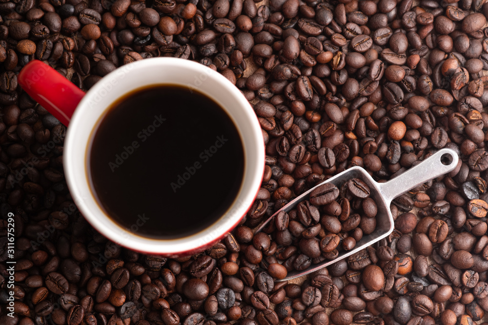 A cup of coffee, coffee beans and metal scoop. Red ceramic mug. A cup of coffee, coffee beans and metal scoop. Red ceramic mug.