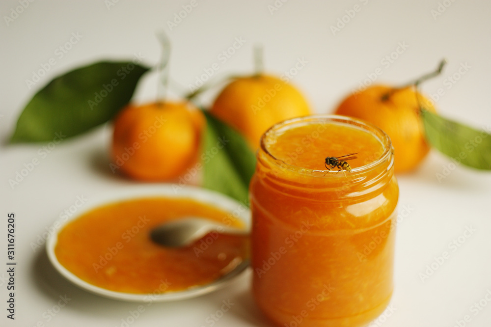 tangerine (mandarin) jam in glass jar on the background of fresh tangerines. bee sits on the edge of a jar of citrus jam