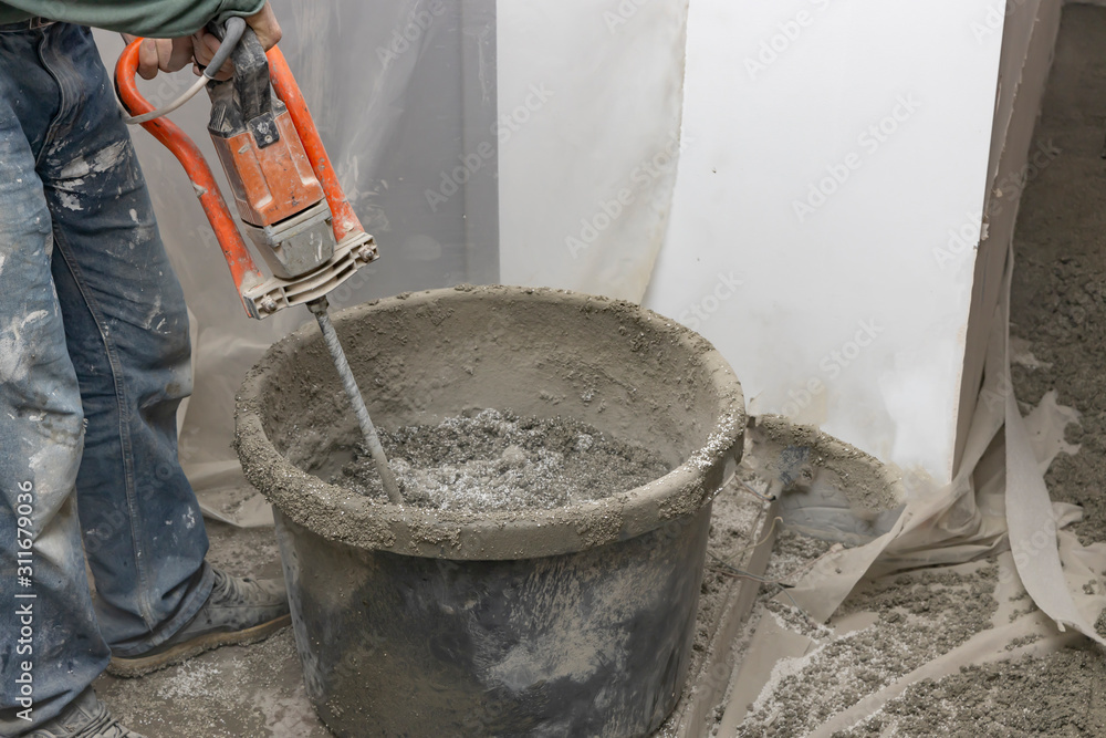 Man kneads cement mortar with a mixer. Floor screed is processed in the apartment. The worker performs a sand-cement floor screed. Man kneads cement mortar with a mixer. Floor screed is processed in the apartment. The worker performs a sand-cement floor screed.