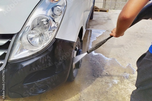 High pressure water jet cleaning. A male car wash's worker washing a white minibus using power sprayer.