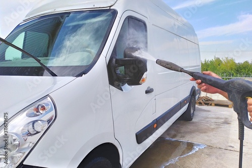High pressure water jet cleaning. A male car wash's worker washing a white minibus using power sprayer.