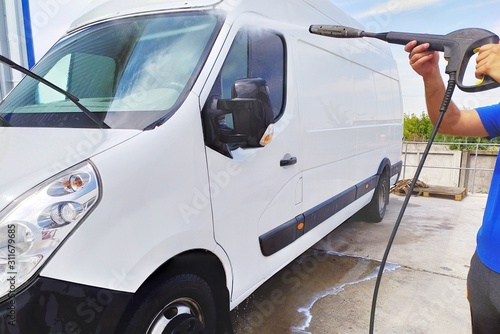 High pressure water jet cleaning. A male car wash's worker washing a white minibus using power sprayer.
