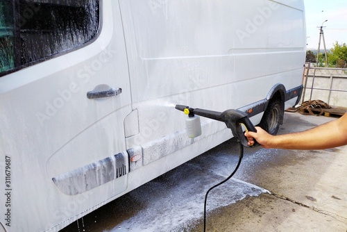 High pressure water jet cleaning. A male car wash's worker washing a white minibus using power sprayer.