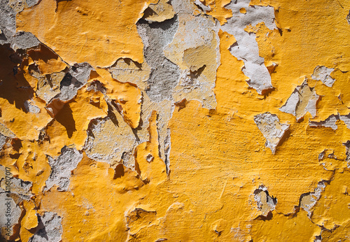 The concrete wall of yellow color is covered with old layers of paint, cracks and texture. Natural light and color. Peeling on the old background.