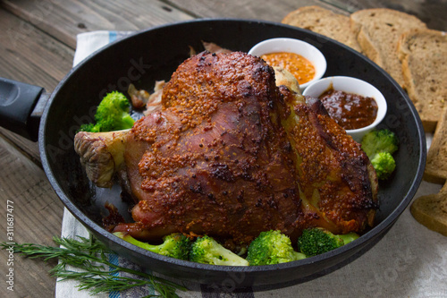 baked pork shank in a pan with vegetables. Bavarian mustard, broccoli