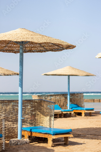 Wooden sun beds by the sea covered with blue towels and with wickered sunshades