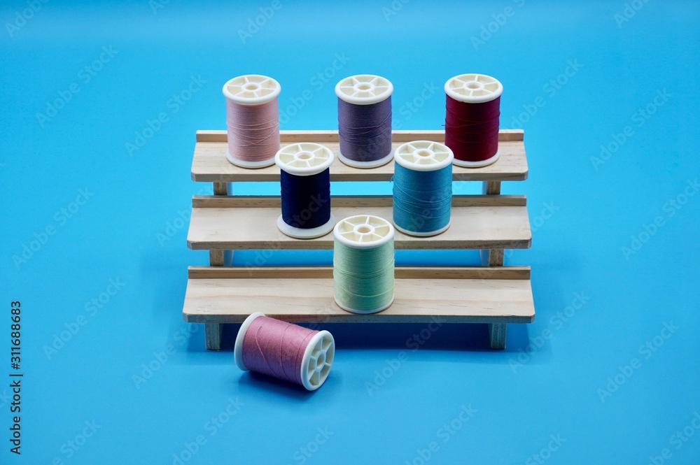A group of pink, purple, red, green, and blue thread on the wooden stand on the blue background A group of pink, purple, red, green, and blue thread on the wooden stand on the blue background