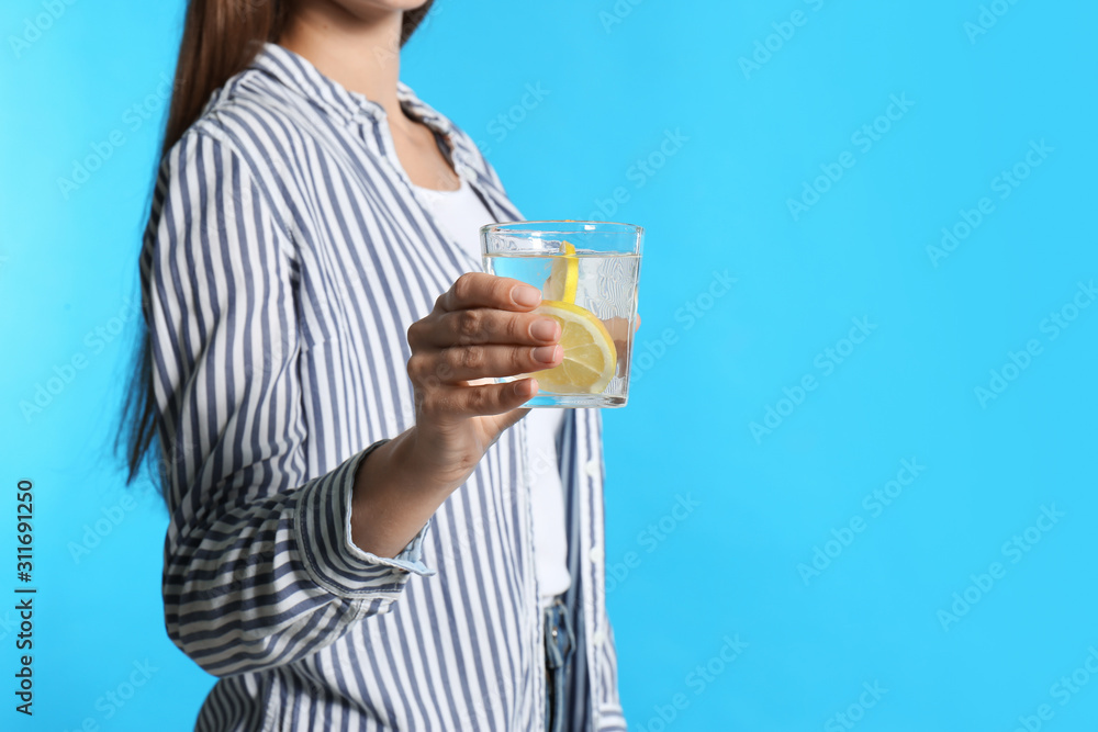 Young woman with glass of lemon water on light blue background, closeup Young woman with glass of lemon water on light blue background, closeup